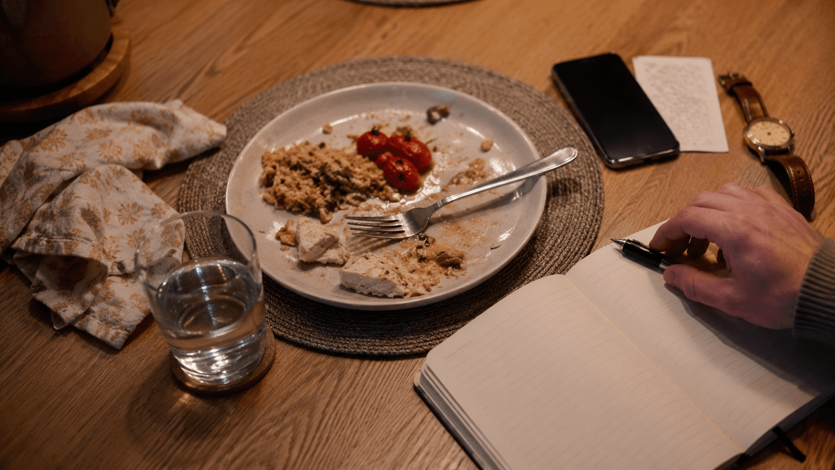 A dinner plate beside a notebook where someone is writing notes after a meal.